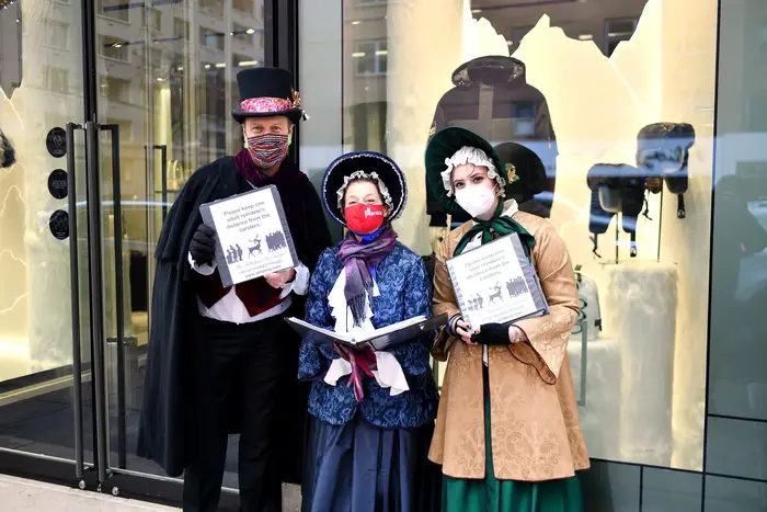 A trio of Christmas carolers outside a store.